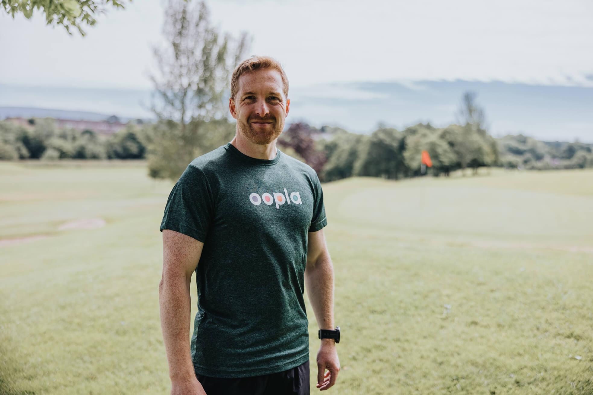 Support to Perform’s CEO Jonny Bloomfield models an Oopla t-shirt on a sports field. 