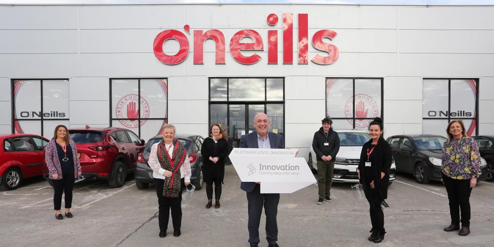 O'Neills staff holding Platinum level innovator badge outside O'Neills factory in Strabane, Co. Tyrone